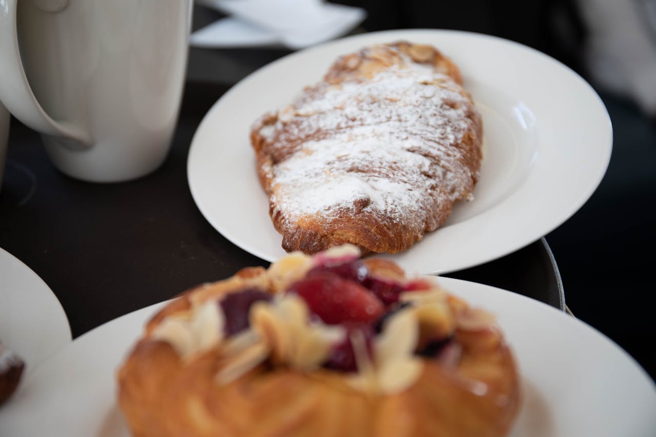A tasty assortment of croissants and pastries with powdered sugar served on white ceramic plates.